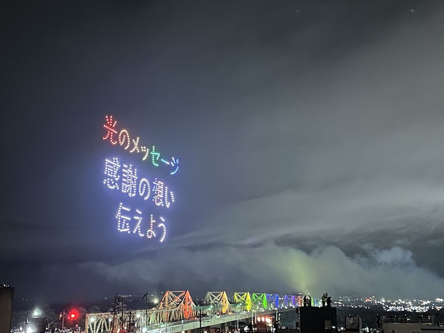 夜空に浮かぶ「光のメッセージ 感謝の想い伝えよう」の文字と、虹色にライトアップされた長生橋